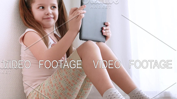 Baby Little Girl Holding And Using Pc Tablet And Sits On The Floor In Room