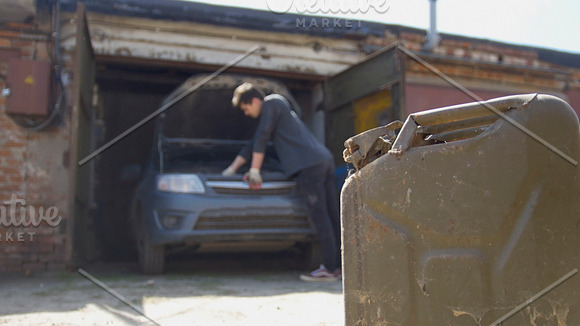 Canister stands in front of young man repairs car in garage in Graphics